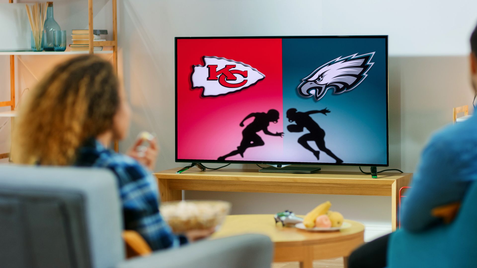 man and woman looking at super bowl team logos on television screen