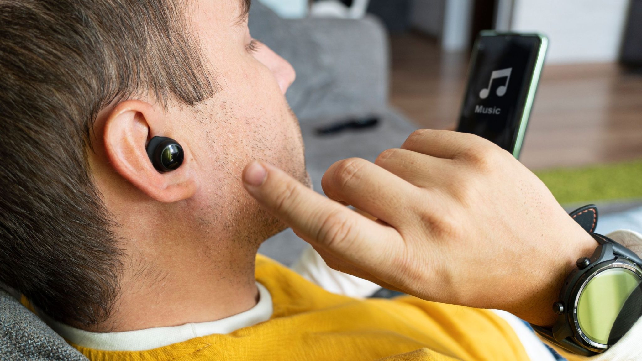 Man wearing earbuds and smartwatch looking at music app on phone